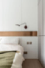 Minimalist bedroom with white walls, copper strip, and modern wall light. Bed with white linens and green throw. Calm and clean ambiance.