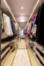 Walk-in closet with organized clothes on both sides, beige drawers open, soft lighting overhead.