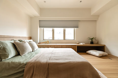 Modern minimalist bedroom design with a cozy bed featuring sage green bedding and neutral pillows. The room is accented by natural wood elements and a large window allowing ample natural light. A stylish plant adds a touch of greenery, creating a serene and inviting atmosphere. Ideal for showcasing contemporary interior design, home decor, and bedroom inspiration.
