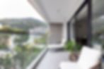 Modern balcony design in Hong Kong apartment featuring sleek glass railings, outdoor lounge chairs, and breathtaking mountain views. Ideal for urban outdoor living, this contemporary space exemplifies luxury interior design, maximizing comfort and style. Perfect for those seeking top interior design services in Hong Kong to transform high-rise apartments into serene retreats.