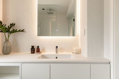 Modern bathroom design featuring a sleek white vanity with an integrated sink and subtle geometric textured wall tiles. The illuminated mirror and minimalist decor, including a green plant and luxury toiletries, create a sophisticated and serene ambiance. Perfect example of contemporary interior design, luxury home decor, and minimalist bathroom aesthetics.