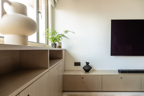 Modern living room interior featuring minimalist wooden cabinetry, decorative vases, and indoor plants near a large window. The sleek flat-screen TV complements the contemporary design, enhancing home aesthetics. Perfect example of functional and stylish interior design for small spaces.
