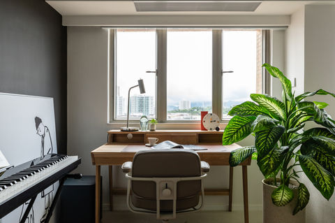 Modern home office interior design featuring a sleek wooden desk with contemporary decor, an indoor plant enhancing the space, and a stylish digital piano against a dark accent wall. Natural light pours in through large windows, creating an inviting and inspiring workspace. Ideal for promoting minimalist design aesthetics and functional home office ideas. 
