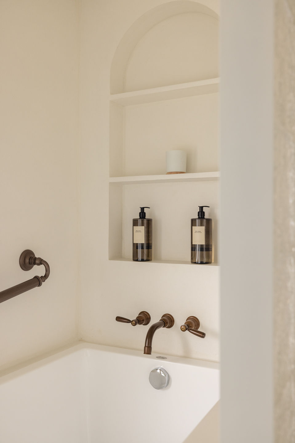 Elegant minimalist bathroom design by MAD Studio featuring a white bathtub with bronze fixtures, built-in shelving, and luxury toiletries. Modern, luxury interior design, bathroom renovation, and contemporary home aesthetics.