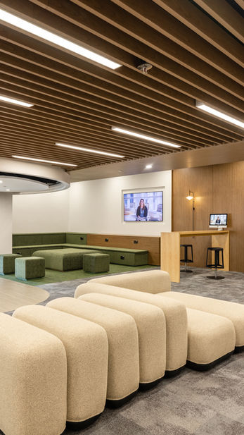 Common Area, VSA, Commercial Interior Design
Parents lounge designed by Mad Studio in a school, featuring modern and comfortable modular seating in beige and green tones. The space includes a ceiling with wooden slats, a media display wall, and bar seating, creating an inviting atmosphere for relaxation and engagement.