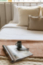 Cozy modern bedroom interior with neutral-toned pillows and a textured throw on a stylish bed. A magazine, pair of glasses, and a coffee mug add a touch of relaxation and comfort. Perfect for an inviting and serene design.