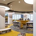 Modern library interior featuring smooth, circular shelving and vibrant yellow accents. The spacious design includes plush seating around contemporary bookshelves, with large, round overhead lights creating a warm ambiance. Perfect for educational and creative spaces, this design promotes a cozy yet functional environment. Keywords: modern library, interior design, vibrant accents, contemporary furniture, creative spaces.