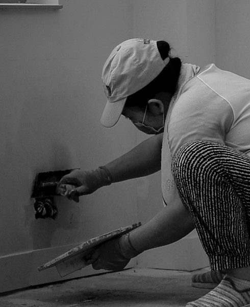 A construction worker painting a section of a wall near an electrical outlet. Pastering a wall section near electric socket